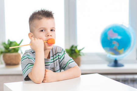 A small child eats a carrot on a stick at home. The boy is eating vegetables in his room.