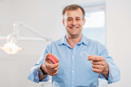 Dental care.Smiling orthodontist doctor holding aligners and braces in hand shows the difference between themの写真素材