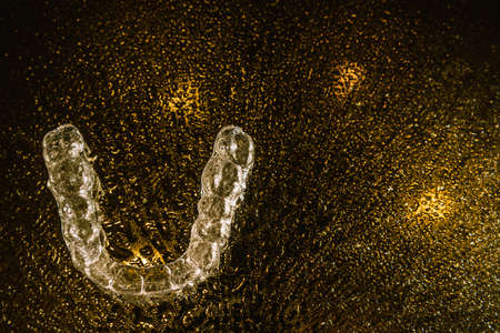 Transparent aligners, tooth retainers lie on glass with water droplets on a black background