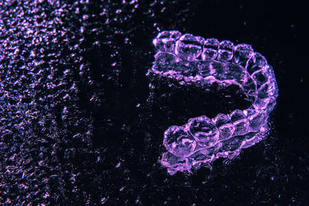 Transparent aligners, tooth retainers lie on glass with water droplets on a black backgroundの写真素材