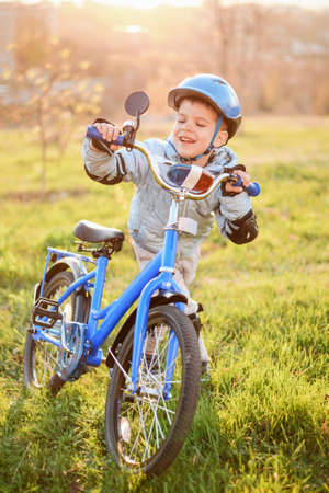 A small child in a helmet leads a bicycle on a sunny day at sunsetの写真素材