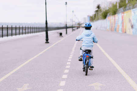 A child in a helmet and protection rides a bicycle on the roadの写真素材