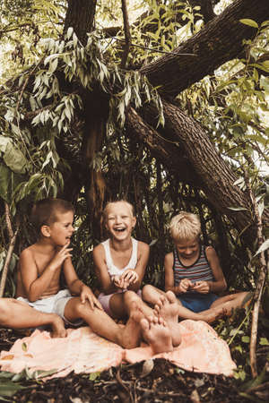 Laughing children play in a hut made of twigs and leaves. Wooden house in the forestの写真素材