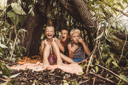 Laughing children play in a hut made of twigs and leaves. Wooden house in the forestの写真素材