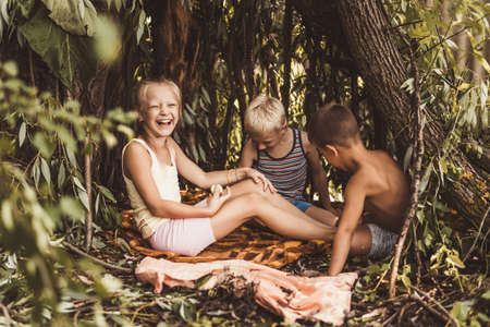 Three children play in a hut which they themselves have built from leaves and twigs.の写真素材