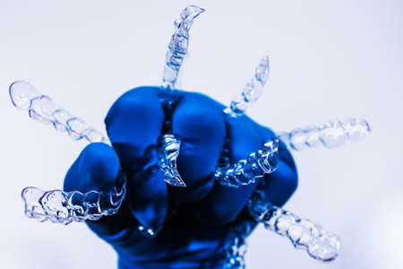 A hand in a blue glove holds aligners for aligning teeth on a white background. Plastic braces dentistry retainers to straighten teeth.の写真素材