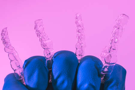 Invisible dental braces are held by a hand in a blue glove on a pink background. Plastic braces dentistry retainers to straighten teeth.の写真素材