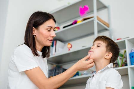 Woman speech therapist training boy to blow correctly using colored feathers exerciseの写真素材