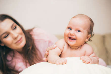 Happy mom with her laughing baby playing in the roomの写真素材