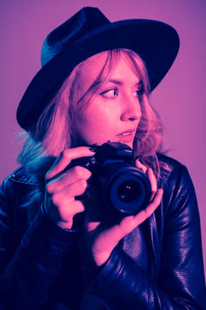 Portrait of a cute girl photographer in a hat who takes pictures in the studio on a fiolet...