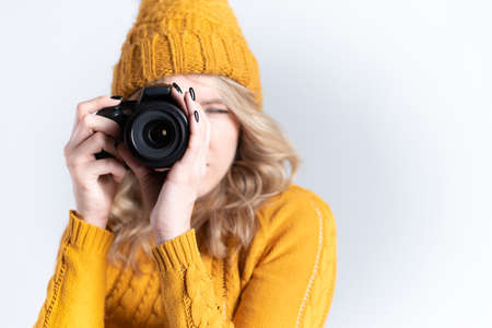 A beautiful woman photographer in a knitted hat is photographed with a camera in her hands in a photo studioの写真素材