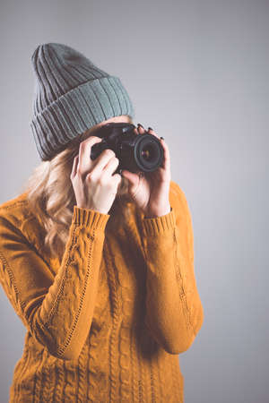 A beautiful woman photographer in a knitted hat is photographed with a camera in her hands in a photo studioの写真素材