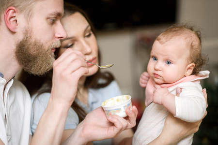 Parents feed their daughter fruit puree in the kitchen