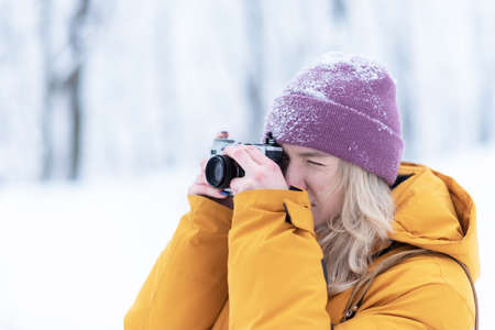 Cheerful girl photographer takes pictures of winter in a snowy parkの写真素材