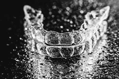 Transparent aligners, tooth retainers lie on glass with water droplets on a black backgroundの写真素材