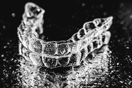 Transparent aligners, tooth retainers lie on glass with water droplets on a black backgroundの写真素材