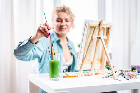 Curly blonde woman painting a picture at home