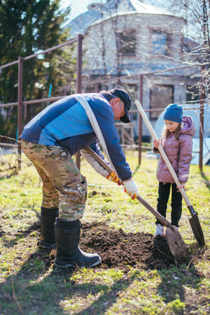 Father teaching his daughter how to plant a new fruit tree in springの写真素材