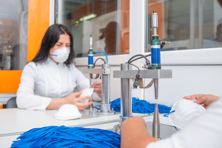 The girl works at the machine for the manufacture of medical masks with nanofibre and solder the loops to them with ultrasound. Coronavirus and Covid-19 Preventionの写真素材