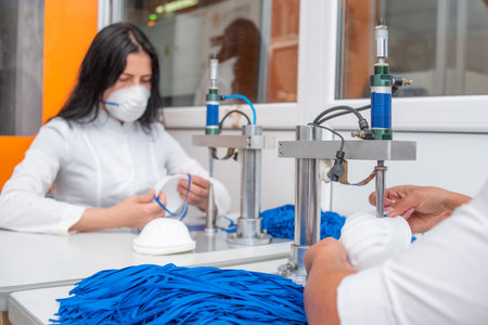 The girl works at the machine for the manufacture of medical masks with nanofibre and solder the loops to them with ultrasound. Coronavirus and Covid-19 Preventionの写真素材