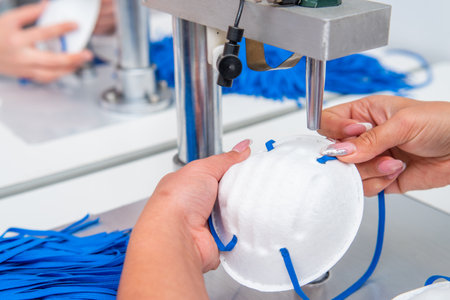 A woman works in a factory for the manufacture of medical masks with nanofibre and solder loops with ultrasound on a machine. Coronavirus and Covid-19 Protection. close-upの写真素材