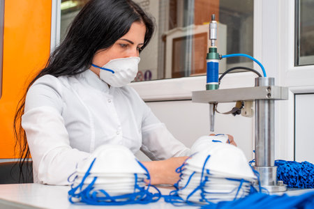 The girl works at the machine for the manufacture of medical masks with nanofibre and solder the loops to them with ultrasound. Coronavirus and Covid-19 Preventionの写真素材