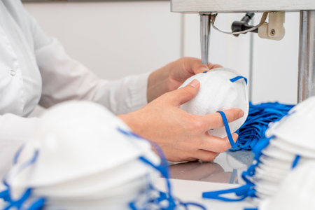 The girl works at the machine for the manufacture of medical masks with nanofibre and solder the loops to them with ultrasound. Coronavirus and Covid-19 Preventionの写真素材