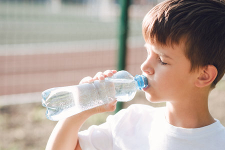 Handsome boy drinks clean water from a bottle on the street in summerの写真素材
