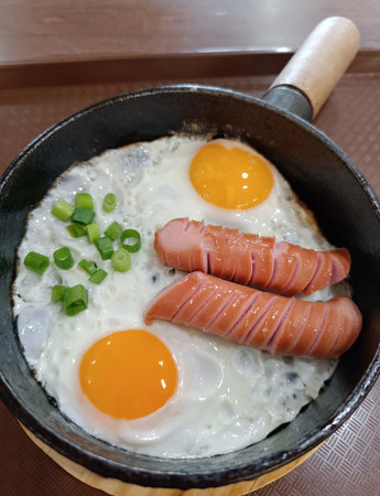 Scrambled eggs in a frying pan with fried meat sausages in a restaurantの写真素材