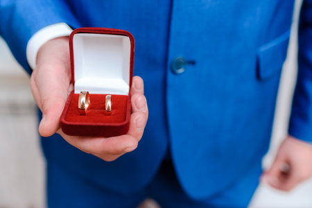 Man groom holding wedding rings in a red box in his hands