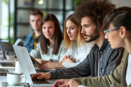 Smiling colleagues discussing a project while working with a laptop in an office indoors. Teamwork in a modern companyの素材