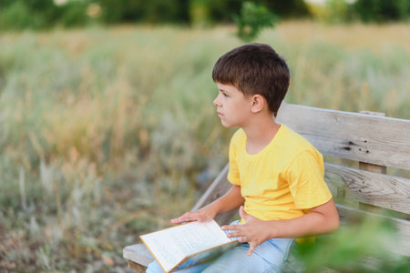 A child reads a book sitting on a bench in natureの写真素材