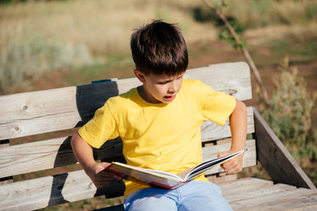 Boy reading a book sitting on a bench in nature during the dayの写真素材