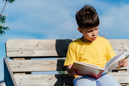 A child reads a book sitting on a bench in natureの写真素材