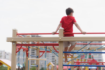 Happy boy playing and hanging on steel bar in playground. Children's exercises for health and concentration in natureの写真素材