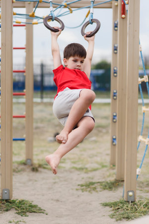Happy boy playing and hanging on rings on playground. Kids exercises for health and concentration