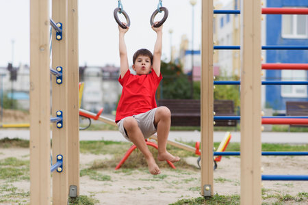Happy boy playing and hanging on rings on playground. Kids exercises for health and concentrationの写真素材