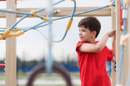 Happy boy playing and hanging on steel bar in playground. Children's exercises for health and...