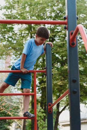 Happy boy playing and hanging on steel bar in playground. Children's exercises for health and...