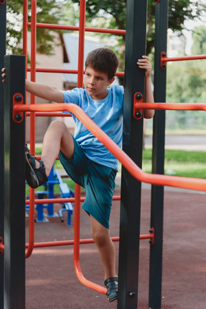 Happy boy playing and hanging on steel bar in playground. Children's exercises for health and...