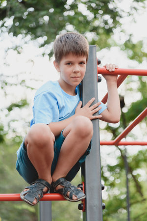 Happy boy playing and hanging on steel bar in playground. Children's exercises for health and concentration in natureの写真素材