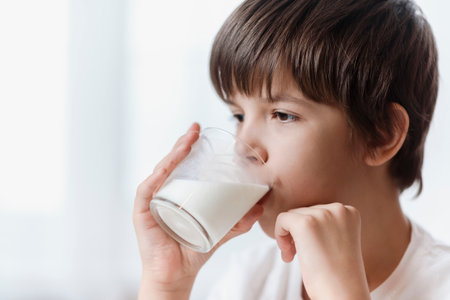 Cute boy drinking milk from glass at home on white backgroundの写真素材