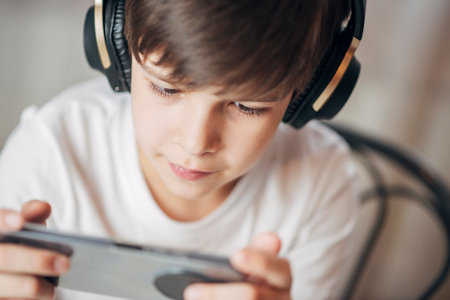 Portrait of a boy with headphones playing games on his phone at home. Happy child looking at his smartphone.の写真素材