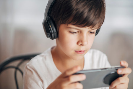 Happy child in headphones playing games on phone at home. Cheerful boy looking at his smartphone.の写真素材