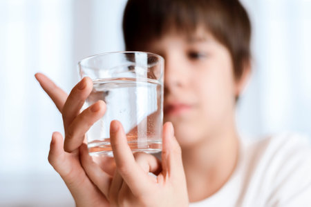 Cute child drinking water from glass at home on white backgroundの写真素材