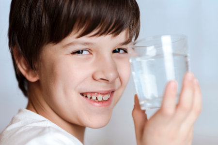 Cute child drinking water from glass at home on white backgroundの写真素材