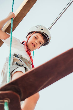 A boy in a rope park in nature learns to rock climb. A child in a helmet walks along a ropeway...
