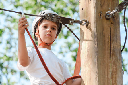 A boy in a rope park in nature learns to rock climb. A child in a helmet walks along a ropeway overcoming obstacles.の写真素材