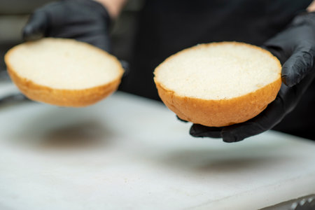 Chef in black gloves prepares burgers with fresh vegetables and sauce.