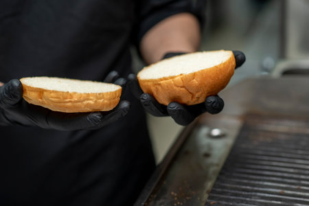 Chef in black gloves prepares gourmet burgers with fresh vegetables and sauce and cutlet in a...